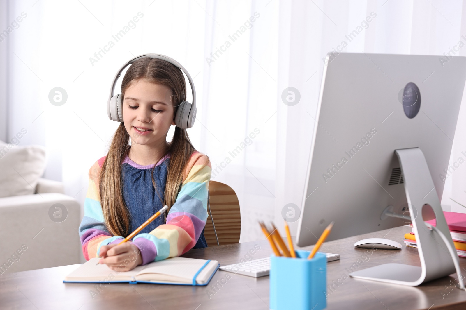 Photo of E-learning. Cute girl taking notes during online lesson at table indoors