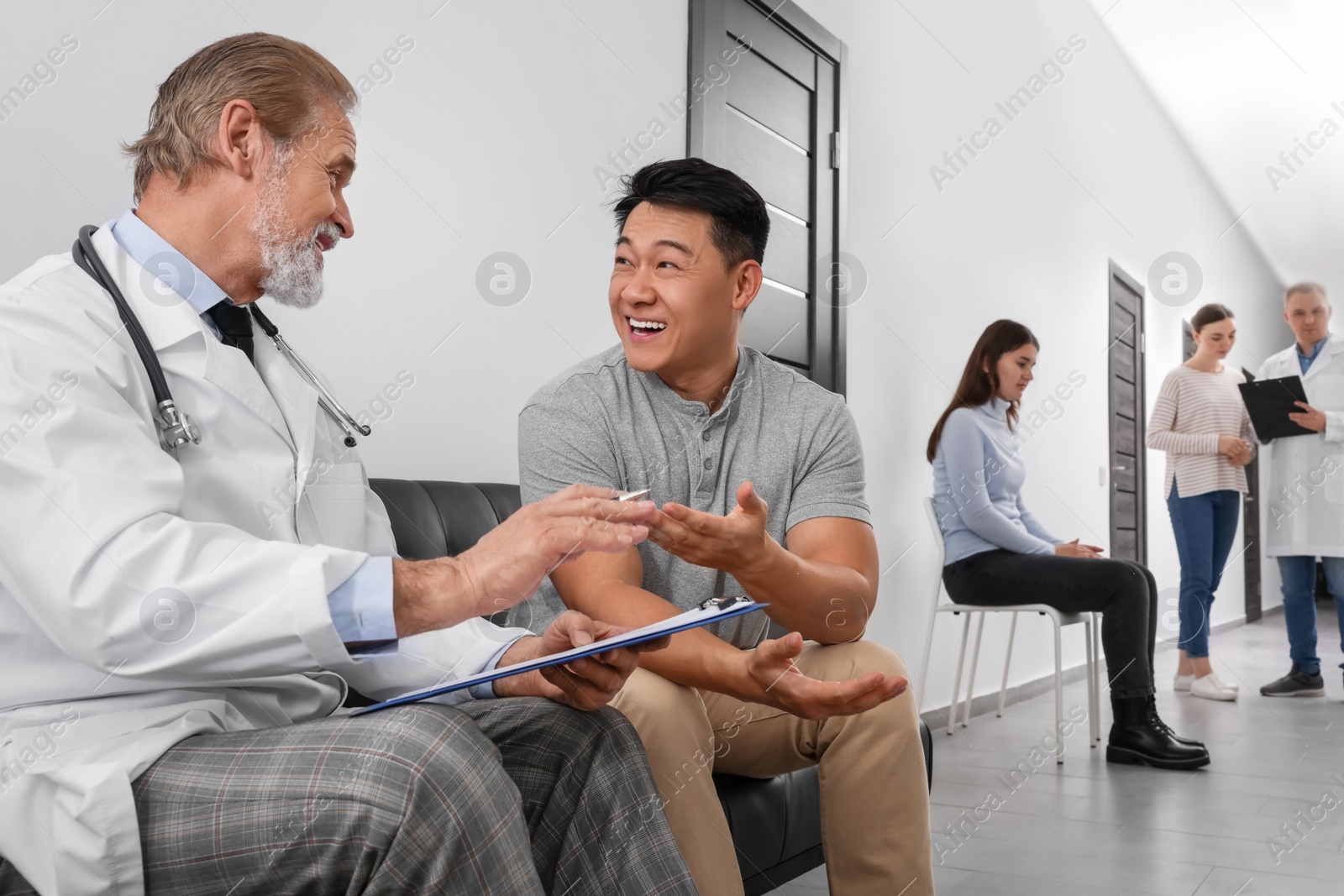 Photo of Senior doctor with clipboard consulting patient in clinic