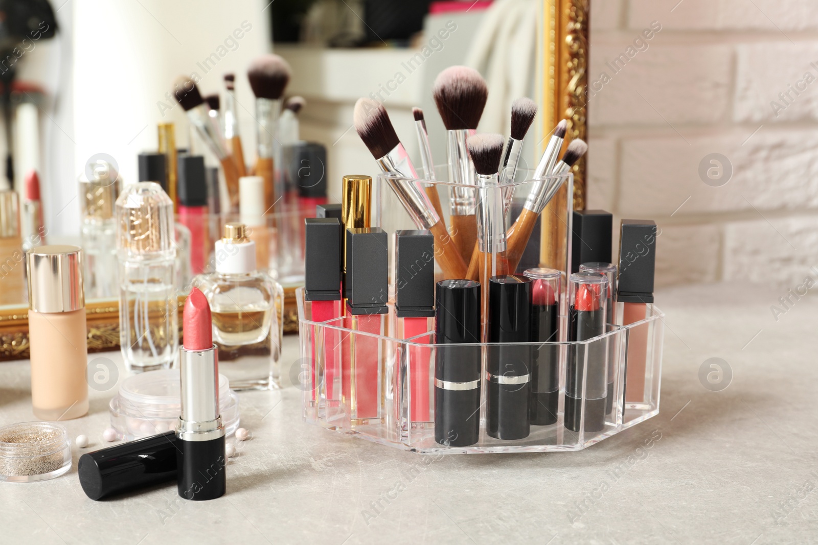 Photo of Lipstick holder with different makeup products on dressing table near mirror