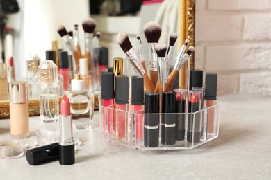 Lipstick holder with different makeup products on dressing table near mirror