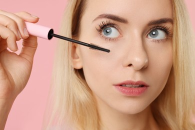 Beautiful woman applying mascara on pink background, closeup