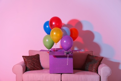 Photo of Gift box with bright air balloons on sofa against color background