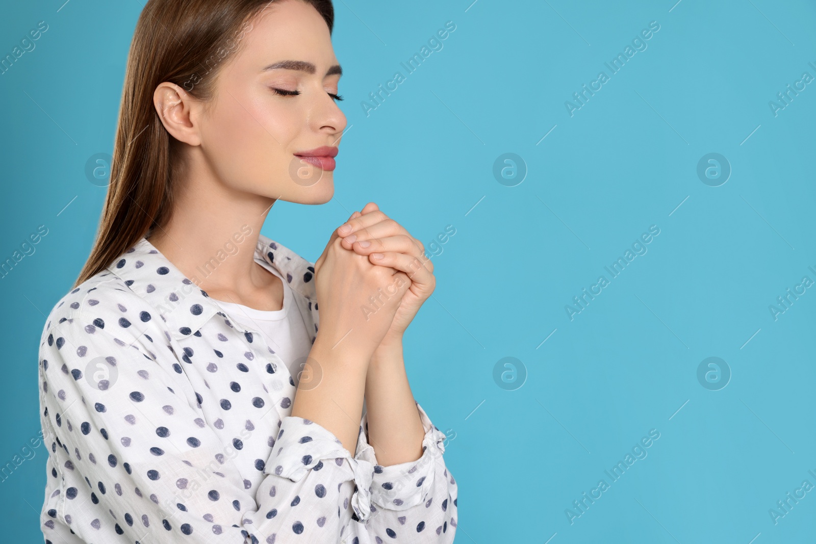 Photo of Woman with clasped hands praying on turquoise background, space for text