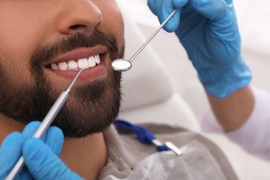 Dentist examining young man's teeth in clinic, closeup