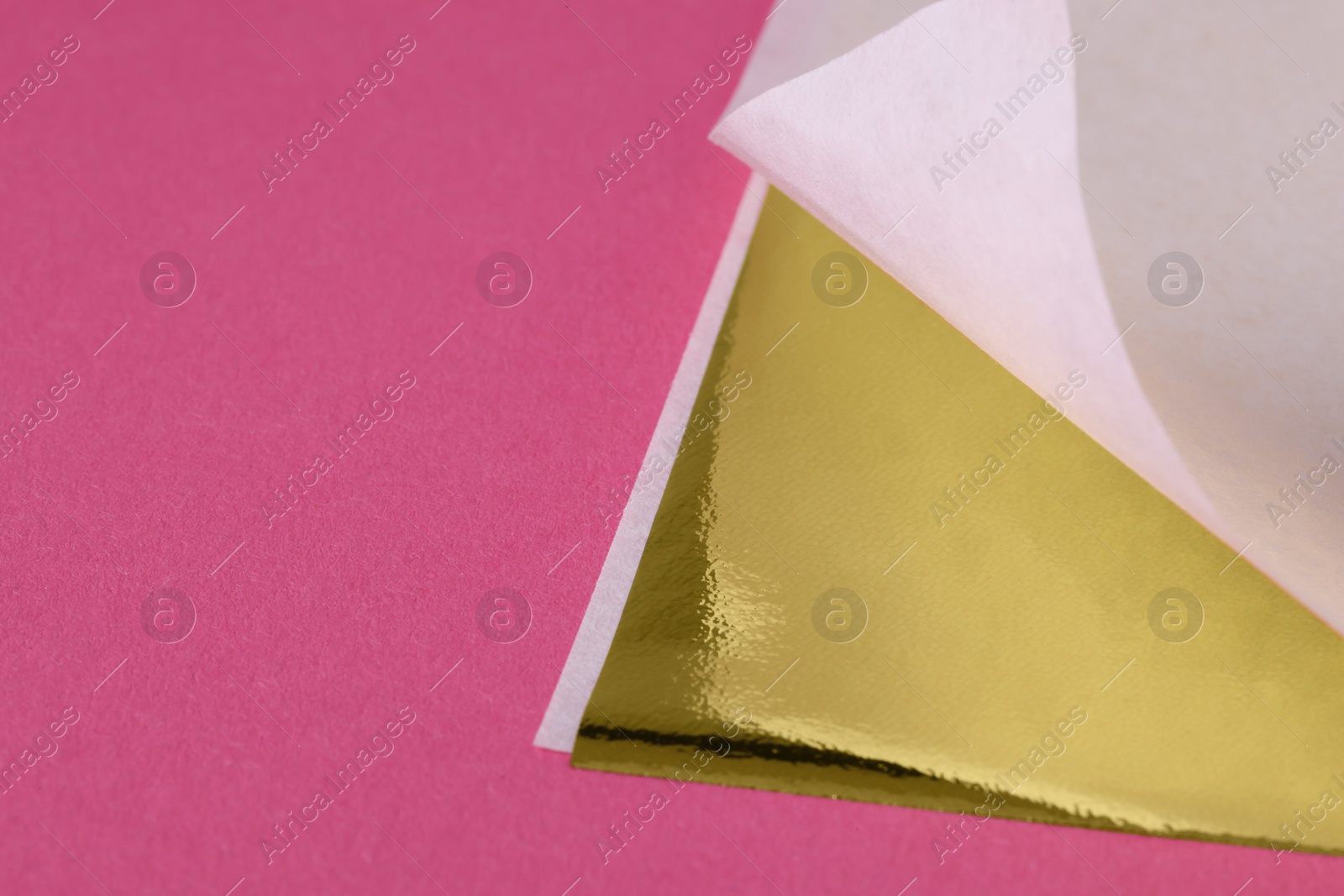 Photo of Edible gold leaf sheet on pink background, closeup. Space for text