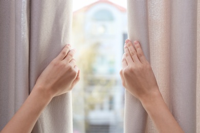 Photo of Woman opening window curtains at home, closeup