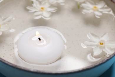 Spa composition with burning candle and beautiful flowers in water, closeup