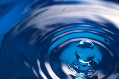 Splash of clear water with drop on blue background, closeup