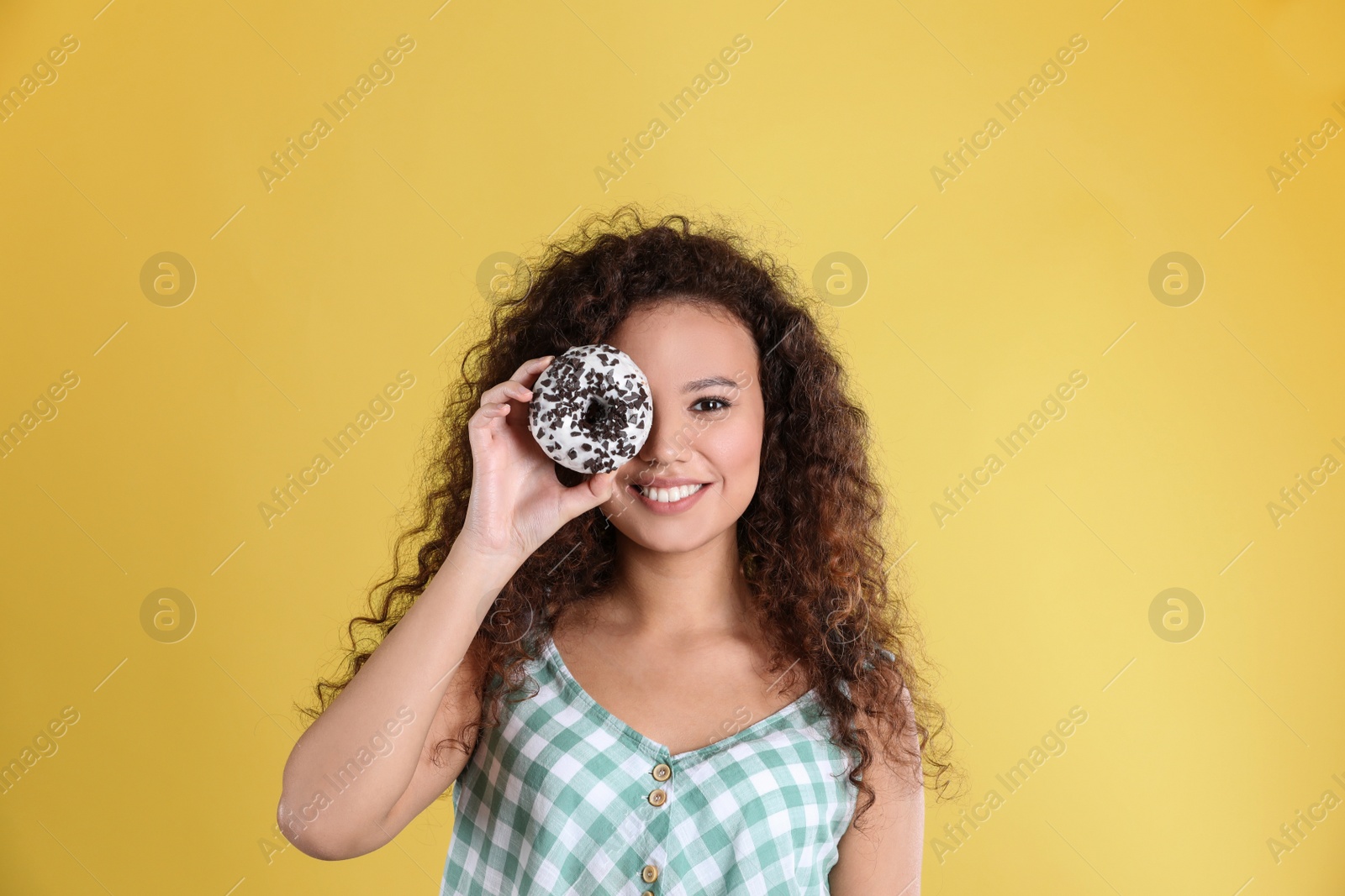 Photo of Beautiful African-American woman with donut on yellow background