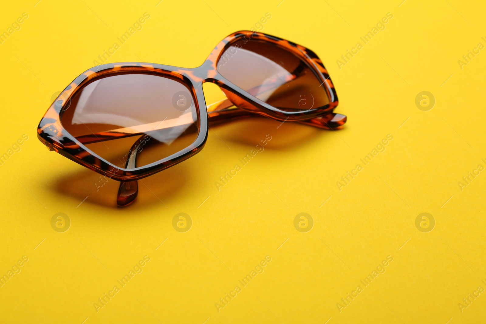 Photo of Stylish sunglasses on yellow background, space for text. Fashionable accessory