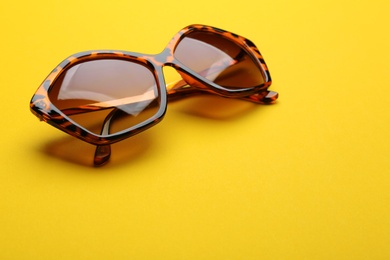 Photo of Stylish sunglasses on yellow background, space for text. Fashionable accessory