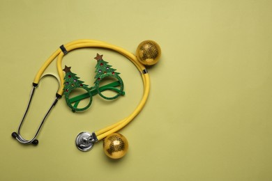 Greeting card for doctor with stethoscope and Christmas decor on green background, flat lay. Space for text