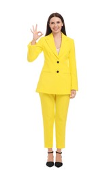 Photo of Beautiful happy businesswoman in yellow suit showing OK gesture on white background