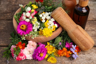 Photo of Bottles with essential oil, mortar, pestle and different flowers on wooden table