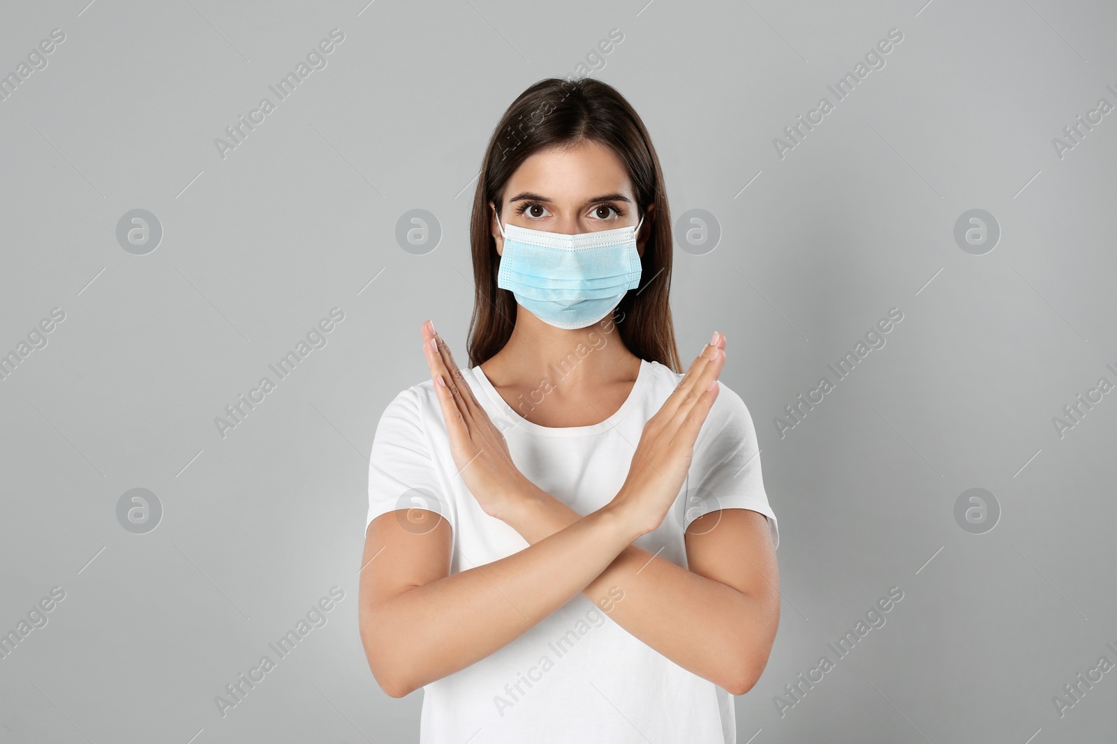 Photo of Woman in protective mask showing stop gesture on grey background. Prevent spreading of coronavirus