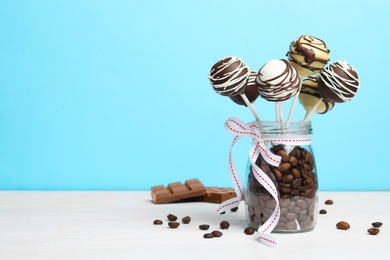 Photo of Glass jar with tasty cake pops and coffee beans on table against light blue background, space for text