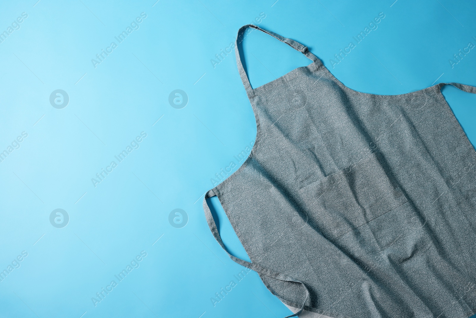 Photo of Grey apron with pattern on blue background, top view. Space for text
