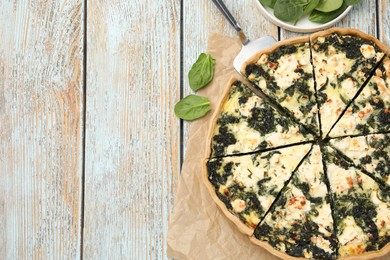 Delicious homemade quiche and spinach leaves on rustic wooden table, flat lay. Space for text