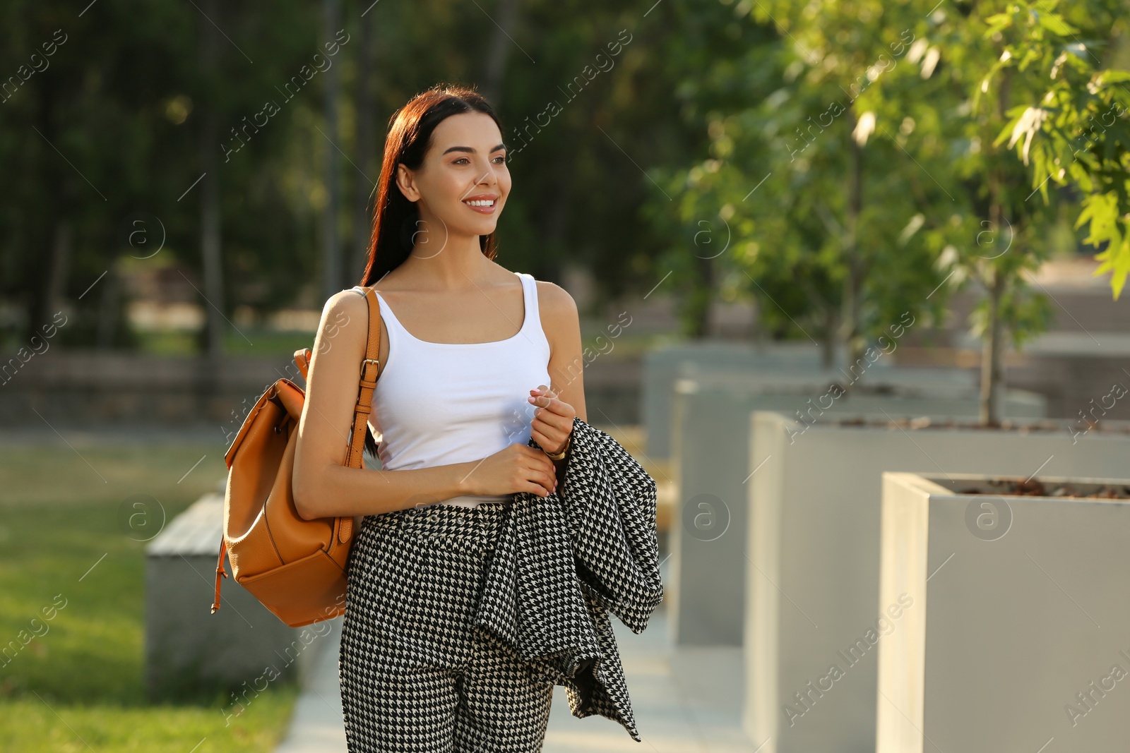 Photo of Beautiful young woman with stylish backpack on city street, space for text