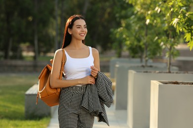 Beautiful young woman with stylish backpack on city street, space for text