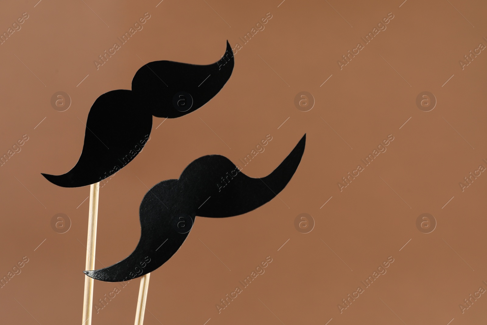 Photo of Fake paper mustaches party props on light brown background, space for text