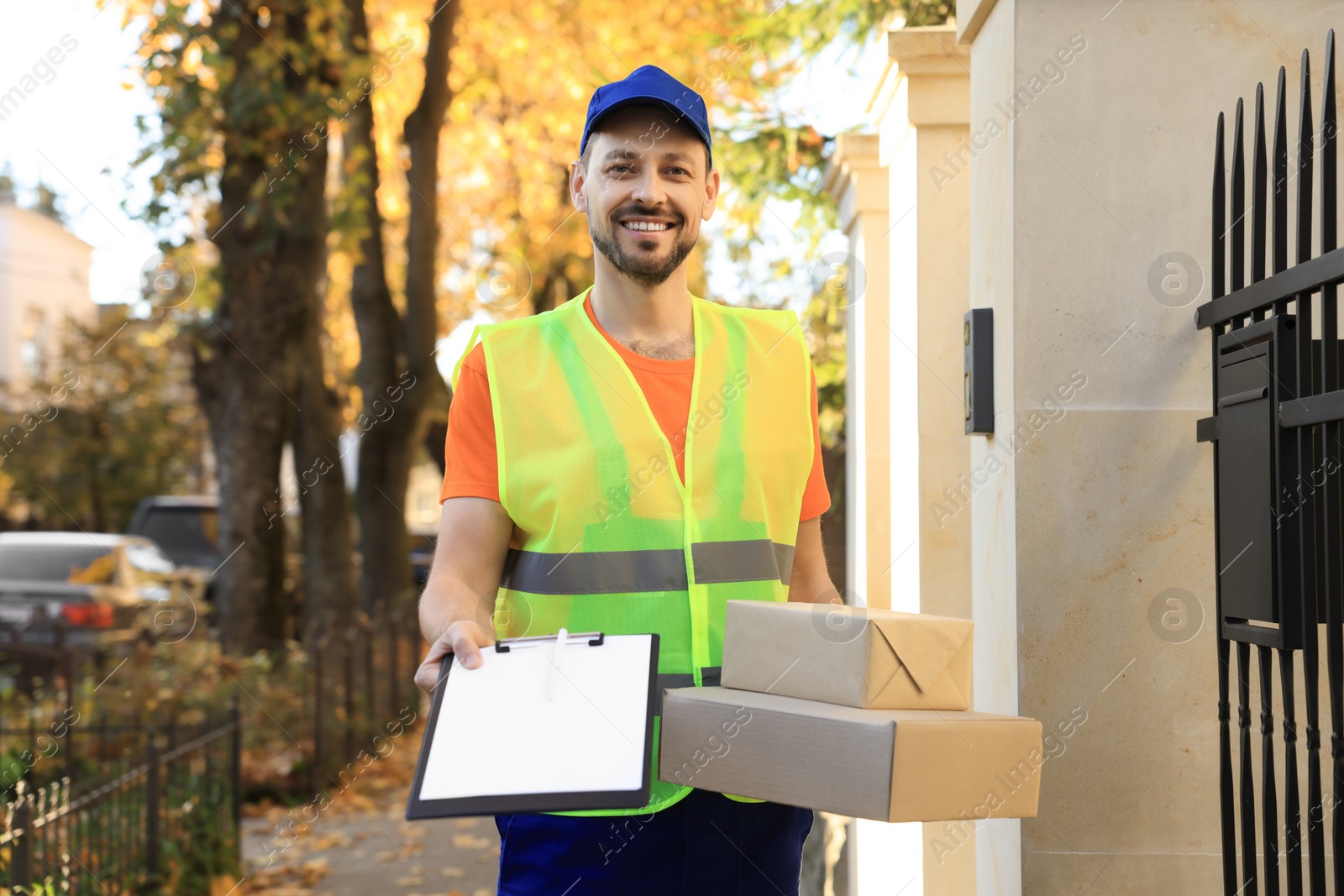 Photo of Courier in uniform holding order receipt and parcels outdoors