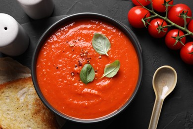 Photo of Delicious tomato cream soup served on black textured table, flat lay