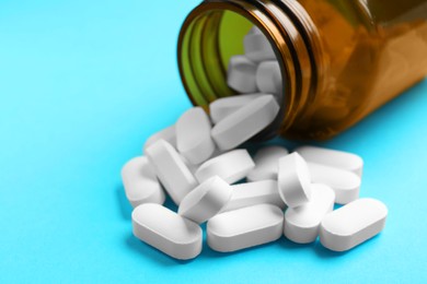 Photo of Bottle and vitamin capsules on light blue background, closeup