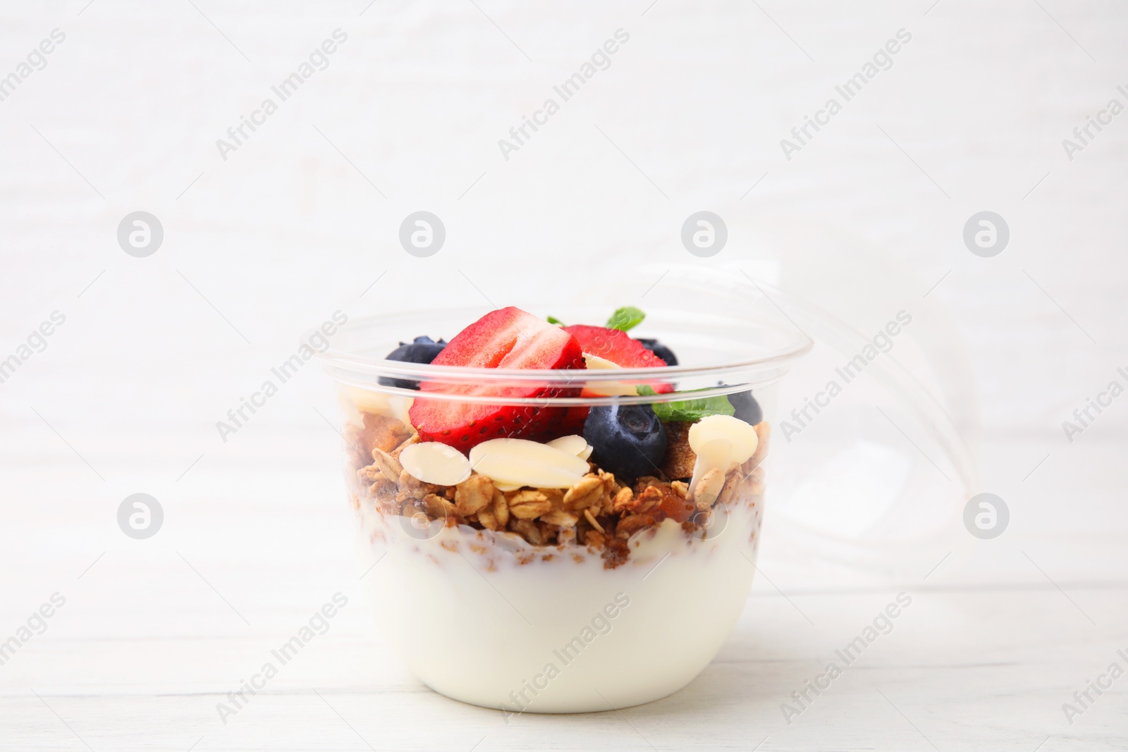 Photo of Tasty granola with berries, yogurt and almond flakes in plastic cup on white table, closeup