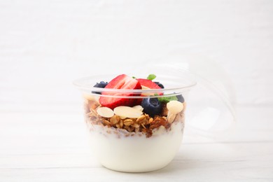 Photo of Tasty granola with berries, yogurt and almond flakes in plastic cup on white table, closeup