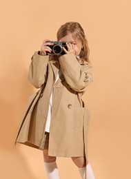 Photo of Fashion concept. Stylish girl with vintage camera on pale orange background