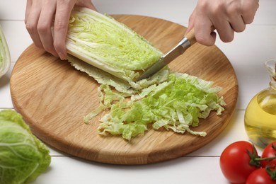 Photo of Woman cutting fresh chinese cabbage at white wooden table, closeup