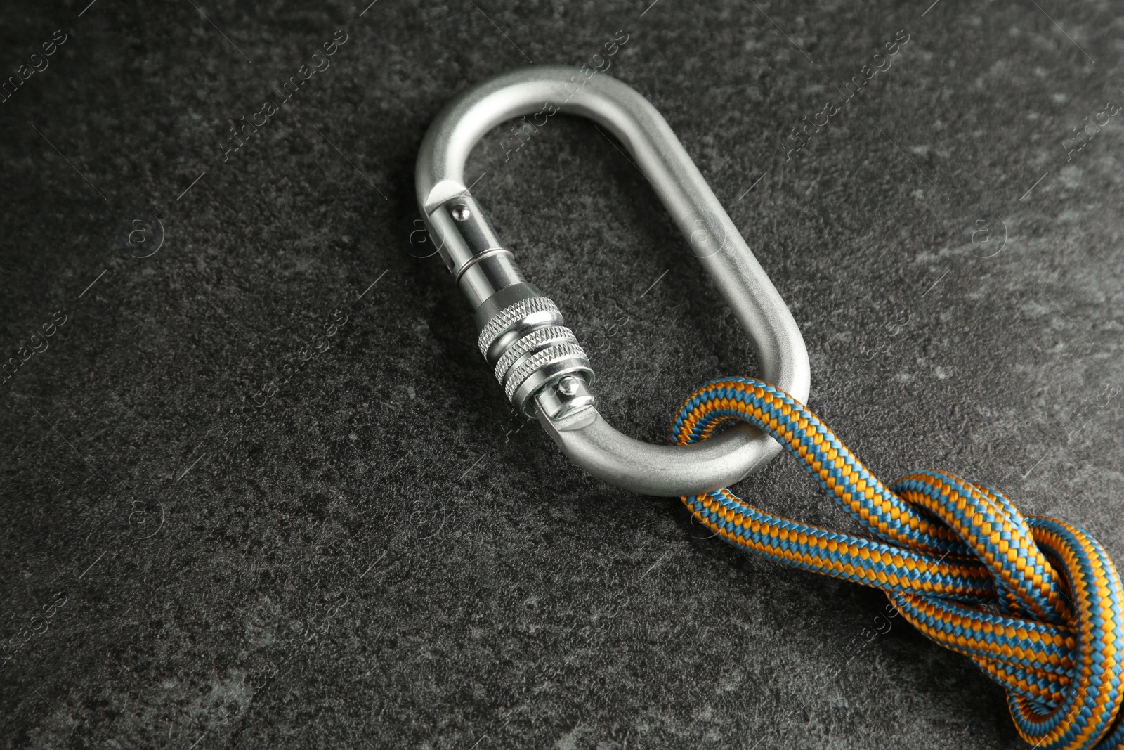 Photo of One metal carabiner with rope on black table, closeup
