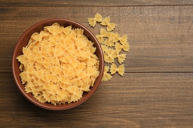 Photo of Raw farfalle pasta in bowl on wooden table, top view. Space for text