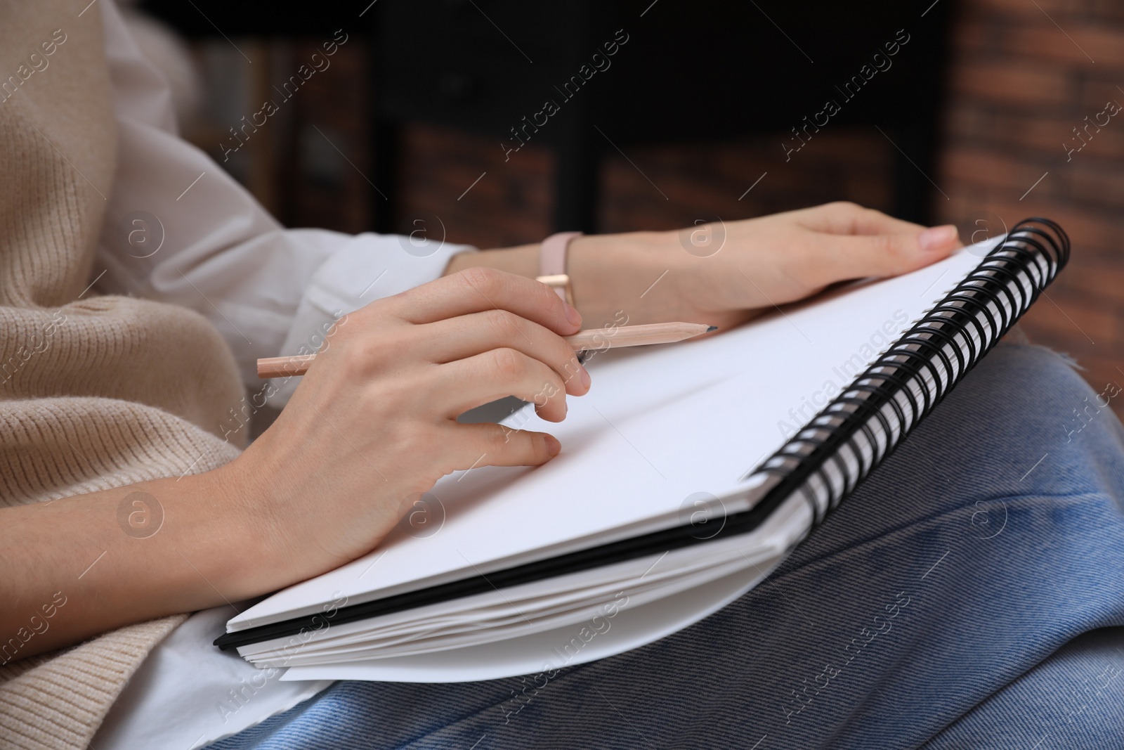 Photo of Woman drawing in sketchbook with pencil at home, closeup