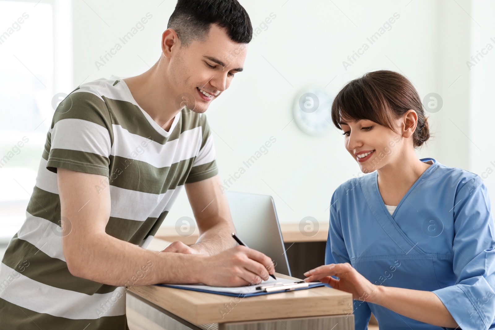 Photo of Smiling medical assistant working with patient at hospital reception