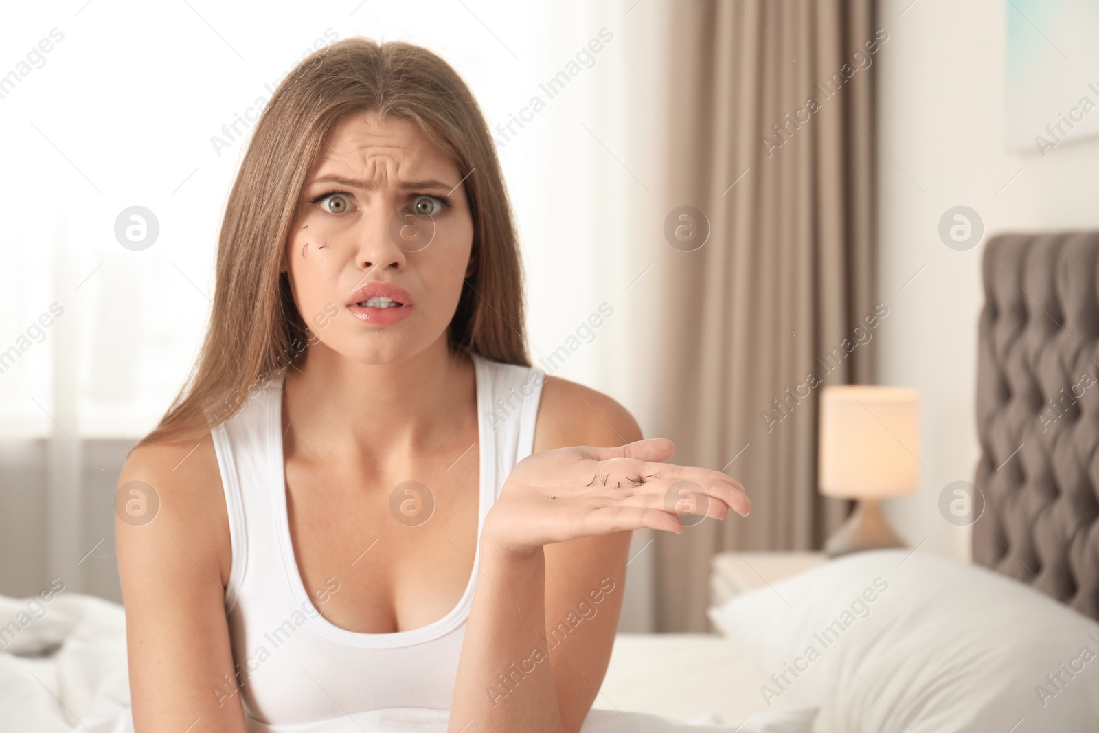 Photo of Emotional young woman holding fallen eyelashes indoors