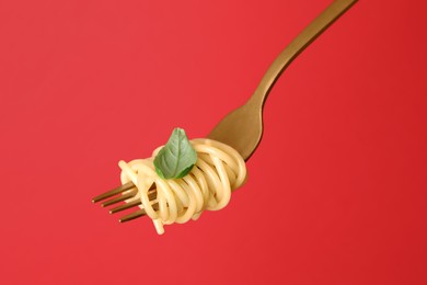 Photo of Fork with tasty pasta and basil on red background, closeup