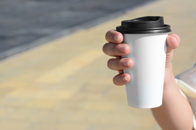 Woman holding takeaway coffee cup outdoors, closeup. Space for text