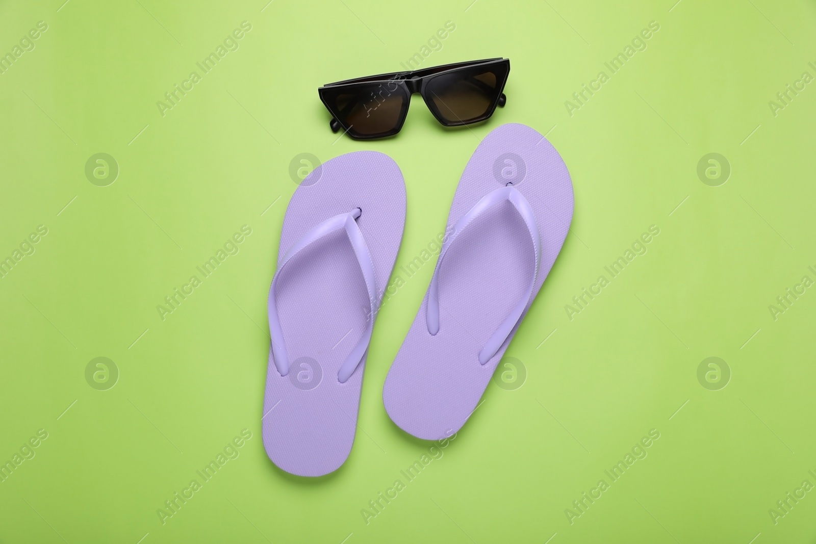 Photo of Stylish flip flops and sunglasses on light green background, flat lay