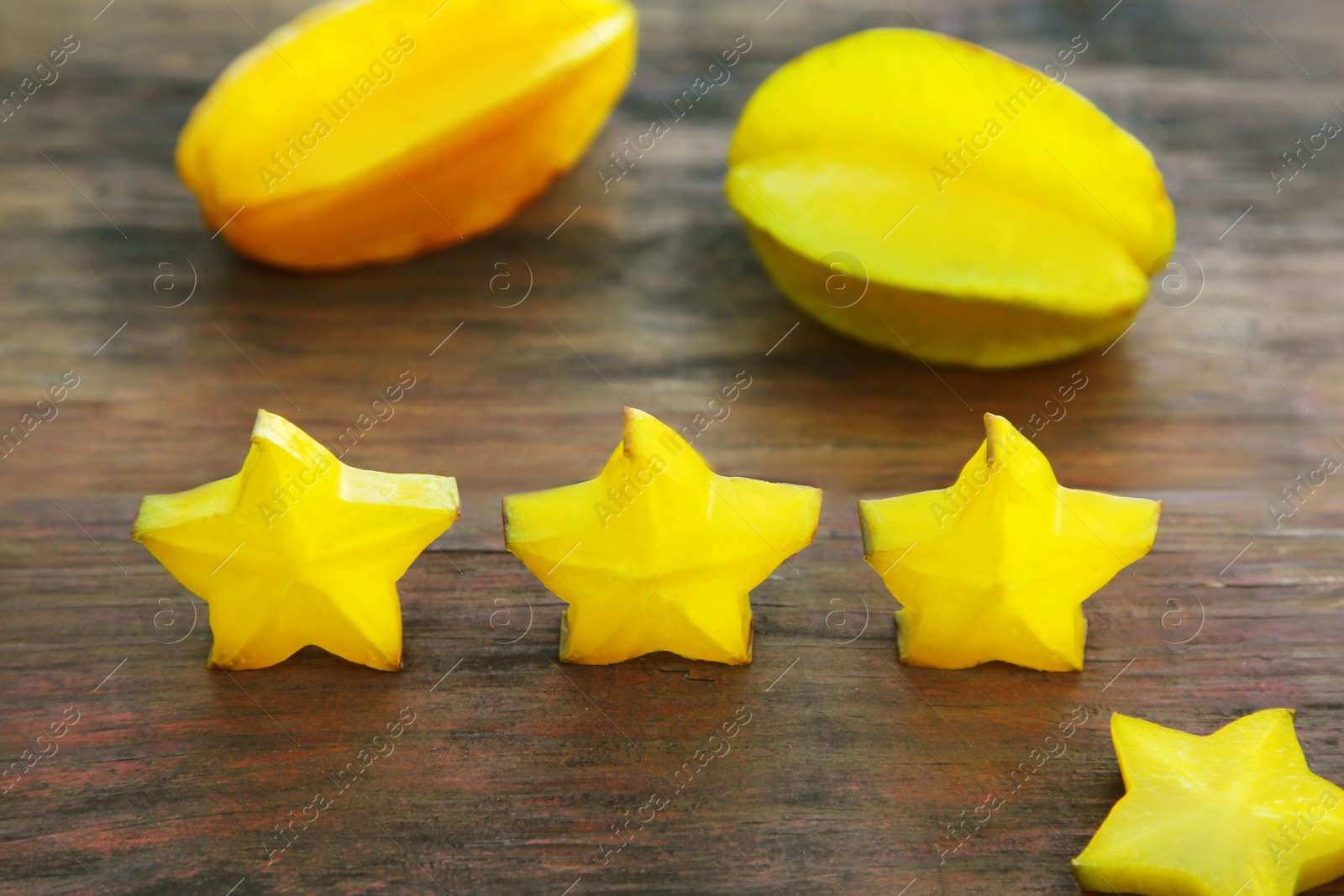 Photo of Delicious cut and whole carambolas on wooden table. Exotic fruit