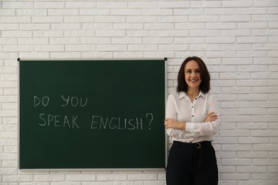 Photo of Teacher near green chalkboard with inscription Do You Speak English? in classroom