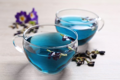 Glass cups of organic blue Anchan on white wooden table, closeup. Herbal tea
