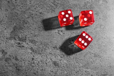 Three red game dices on grey textured table, flat lay. Space for text