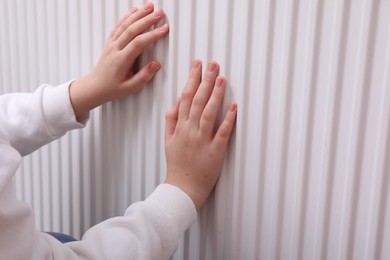 Girl warming hands on heating radiator, closeup