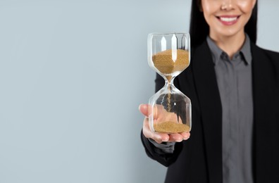 Photo of Businesswoman holding hourglass on light grey background, closeup with space for text. Time management