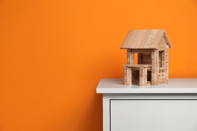 Photo of Wooden house on white chest of drawers near orange wall, space for text. Children's toy