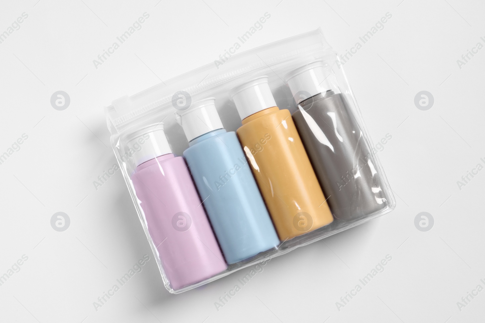 Photo of Cosmetic travel kit in plastic bag on white background, top view