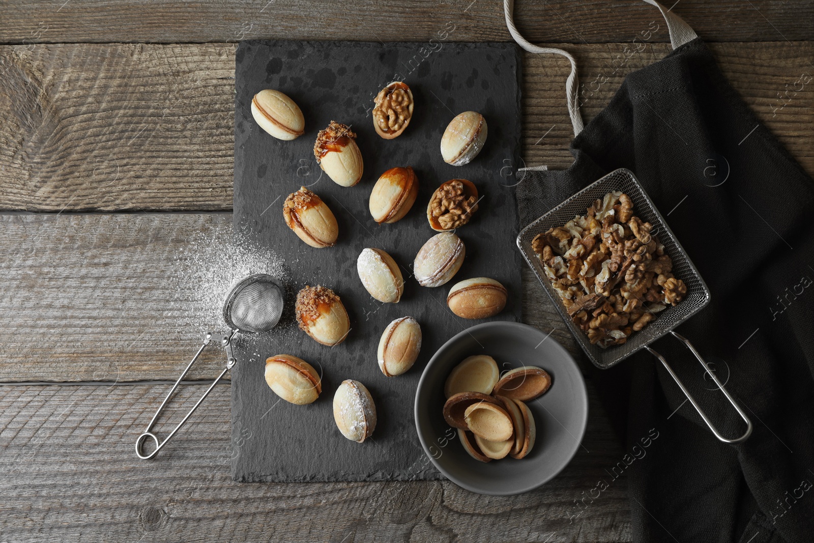 Photo of Freshly baked homemade walnut shaped cookies, nuts and flour on wooden table, flat lay