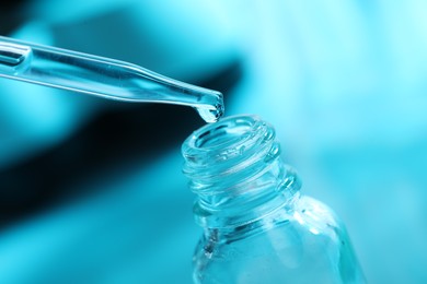 Photo of Dripping liquid from pipette into glass bottle on light blue background, closeup